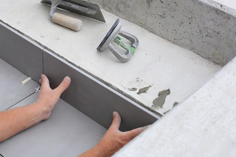 a person is laying tiles on a concrete surface .