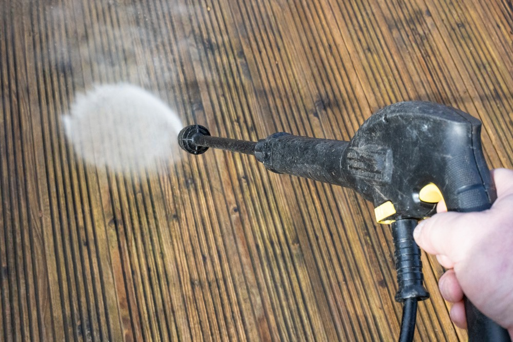 a person is using a high pressure washer to clean a wooden deck .