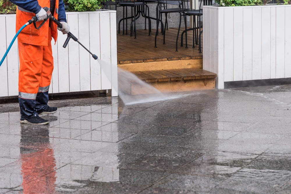 a man is using a high pressure washer to clean a sidewalk .