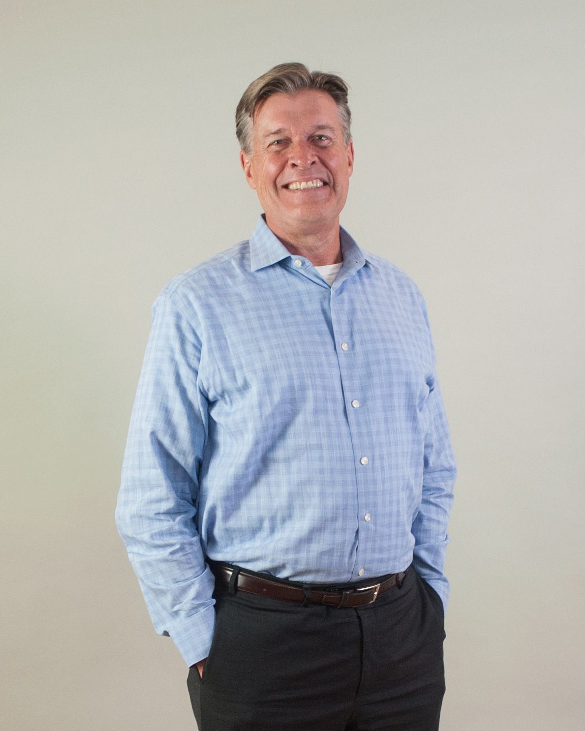 A man in a blue shirt and black pants is standing with his hands in his pockets.