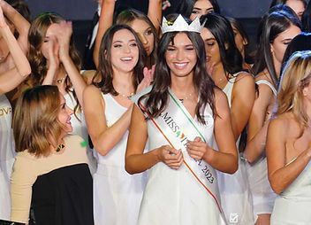 Un gruppo di donne è in piedi attorno a una donna che indossa una corona e una fascia.