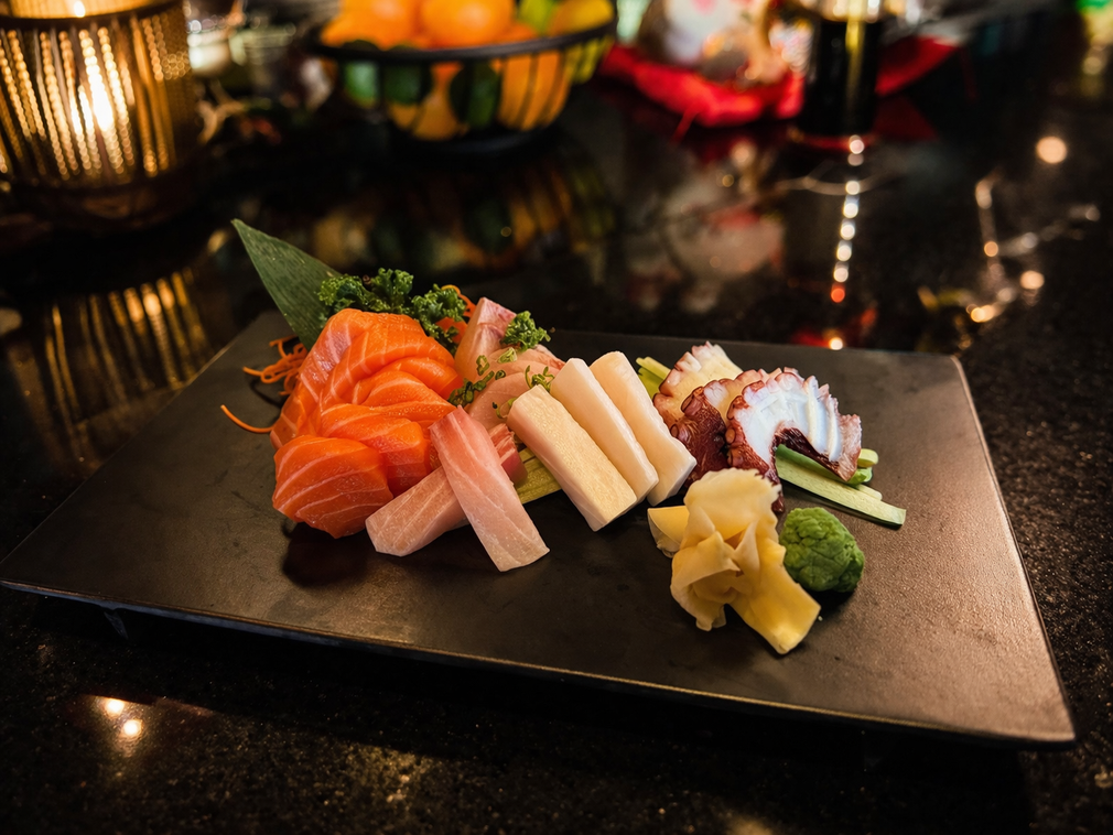 A sashimi platter with salmon, white fish, and octopus, served with pickled ginger and wasabi on a dark slate plate.
