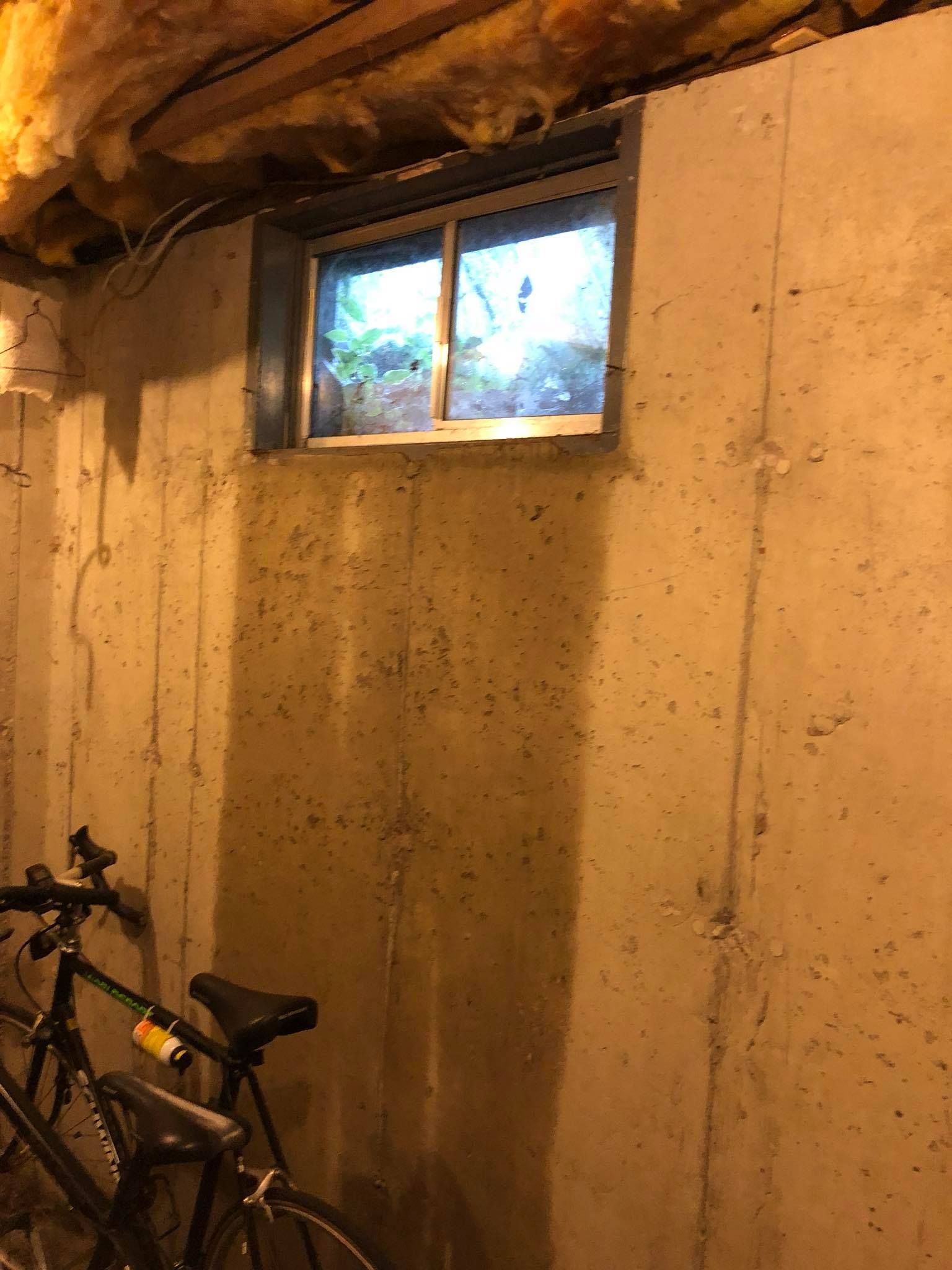 A bicycle is parked in a basement next to a window.