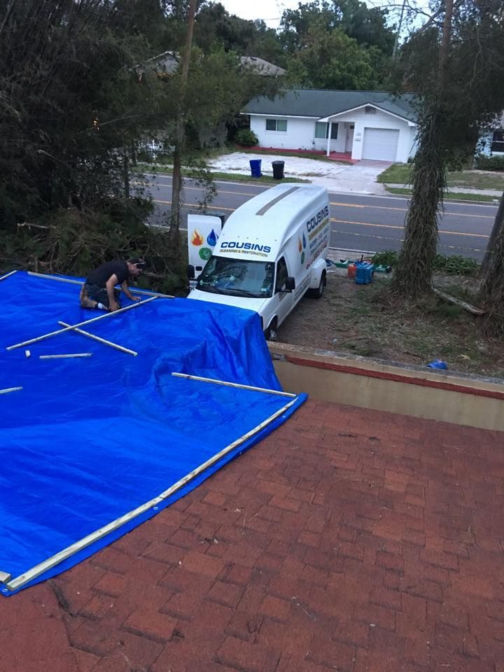 A white van is parked on a roof with a blue tarp on it.
