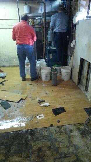 Two men are standing in a room with buckets on the floor.
