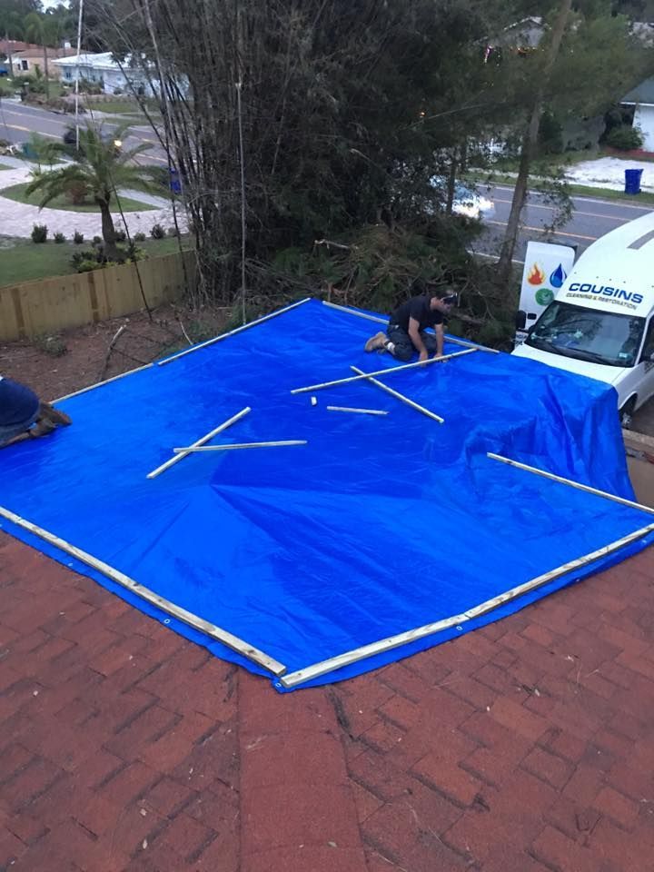 A man is laying on a blue tarp on top of a roof.