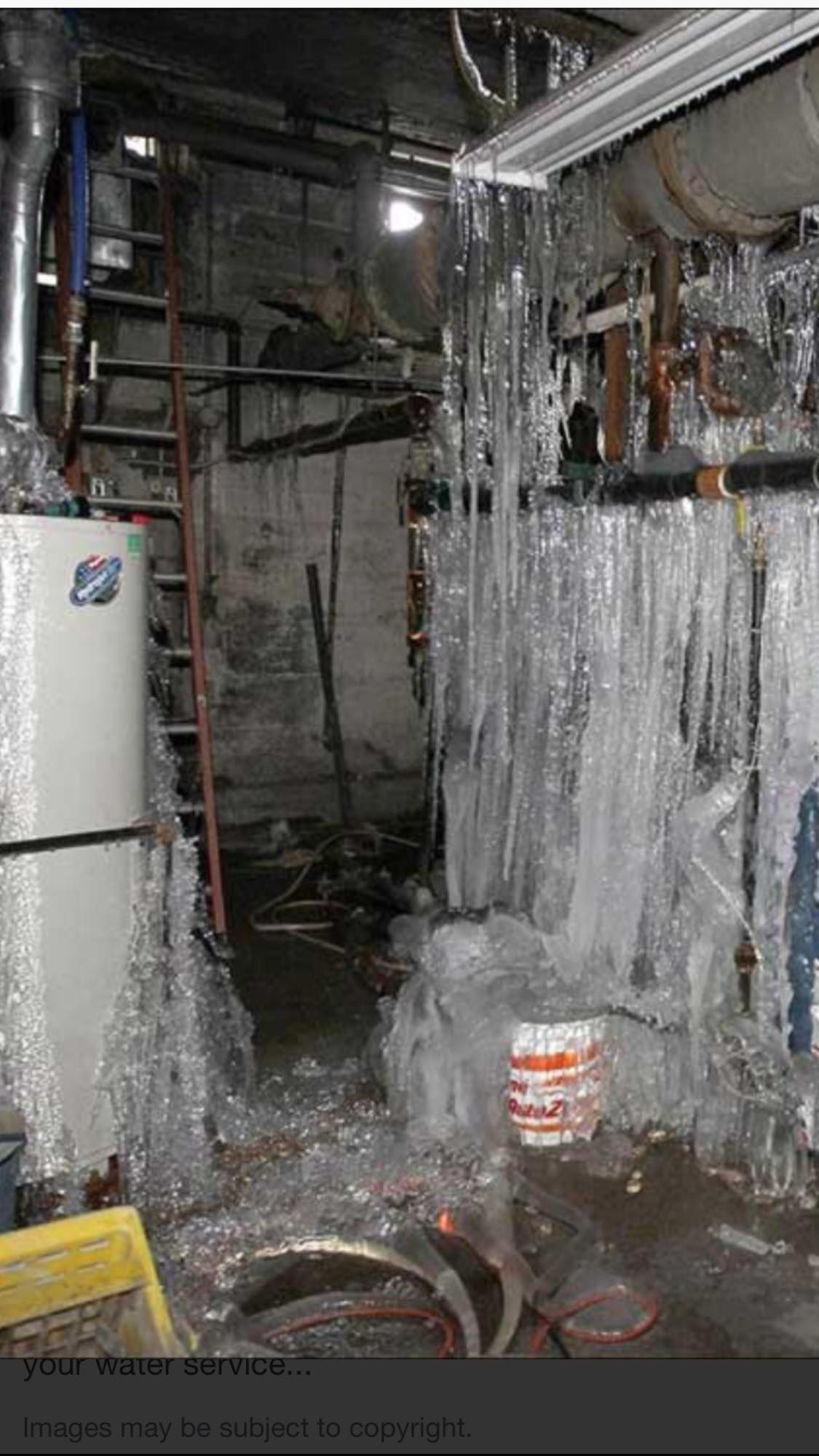 A basement with icicles hanging from the ceiling and a refrigerator.