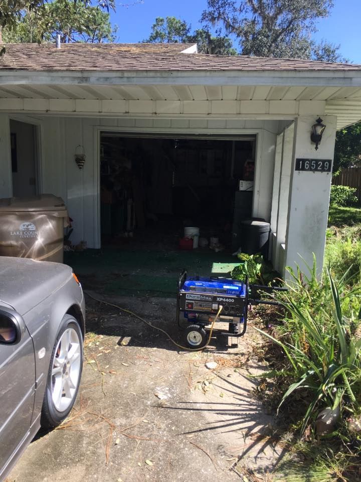 A car is parked in front of a house with a generator in the driveway.