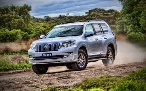 A silver toyota land cruiser is driving down a dirt road.