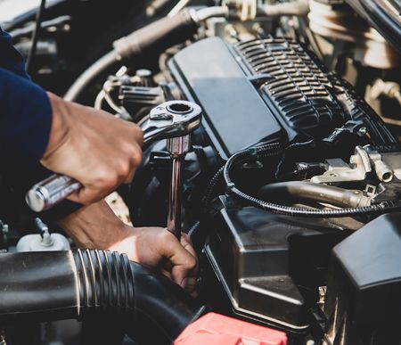 A man is working on a car engine with a wrench.