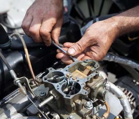 A man is working on a carburetor with a screwdriver