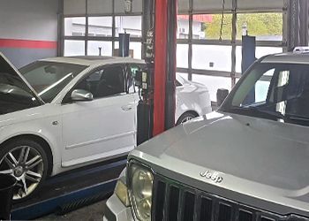 Two cars are sitting on a lift in a garage.