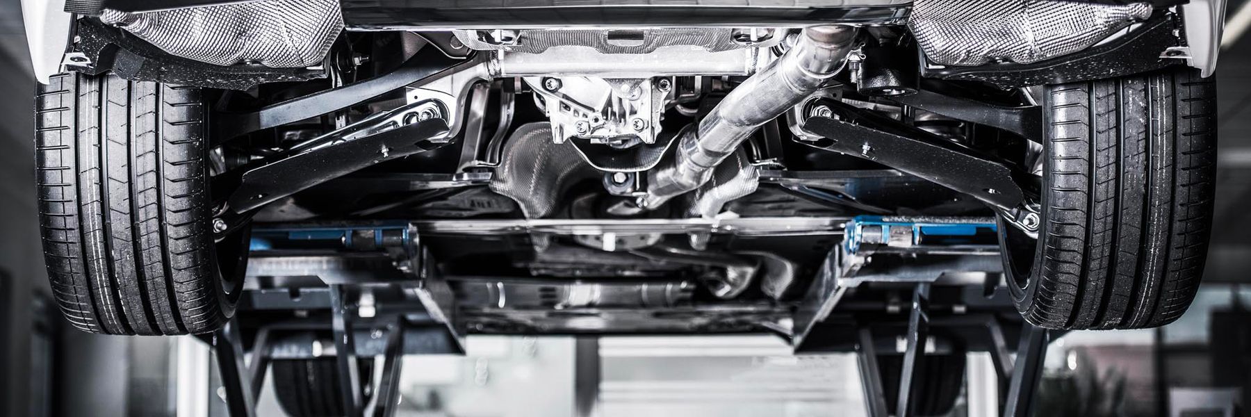 Undercarriage of a vehicle, viewed from below. Tires, suspension, and exhaust system are visible.