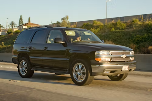 Dark green SUV driving on a sunlit road, side view.