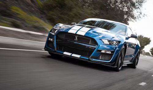 Blue Shelby Mustang sports car driving on a road with white racing stripes.