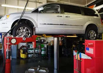Silver minivan on a hydraulic lift in a garage, with tools and equipment visible.