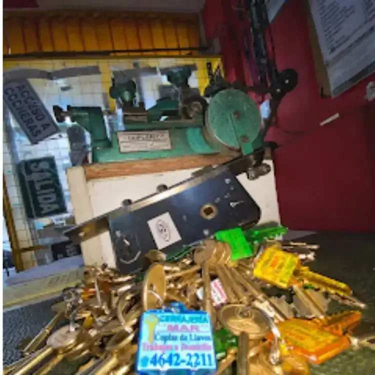 Un montón de llaves de latón surtidas descansa sobre un mostrador debajo de una máquina duplicadora de llaves de metal verde.