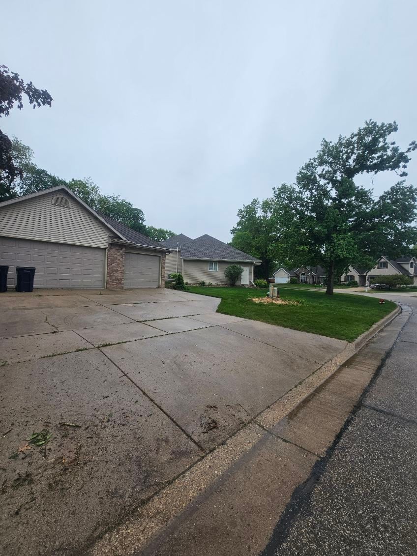 A concrete driveway leading to a house on a cloudy day.