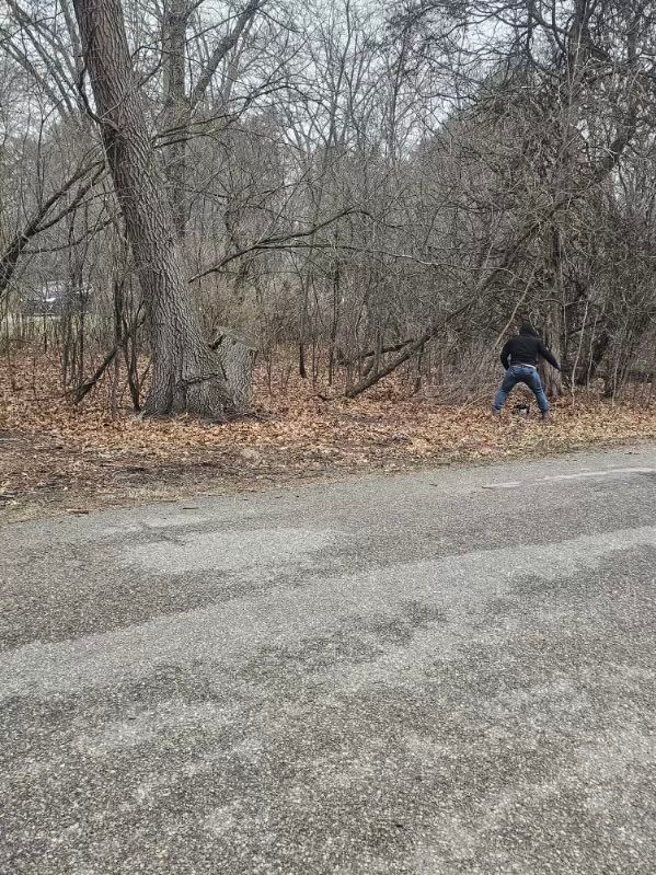 A man is standing on the side of a road in the woods.