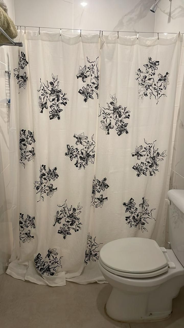 Cortina de ducha con diseño floral negro frente a un inodoro. La cortina es blanca. El baño tiene paredes claras.