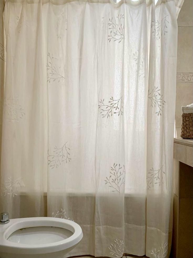 Cortina de ducha de color crema con bordado floral en un baño, ocultando parcialmente el inodoro.