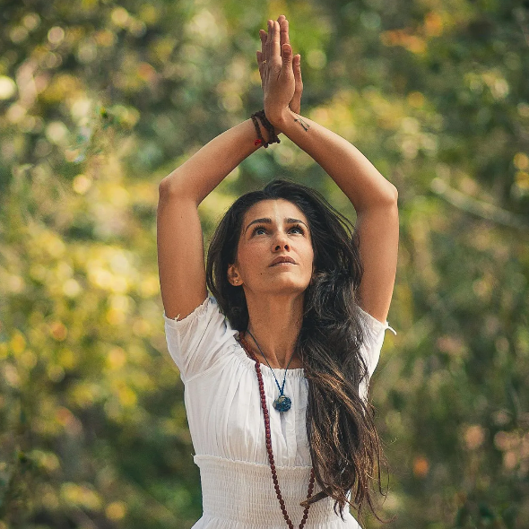 A woman in a white dress is doing a yoga pose with her hands in the air.