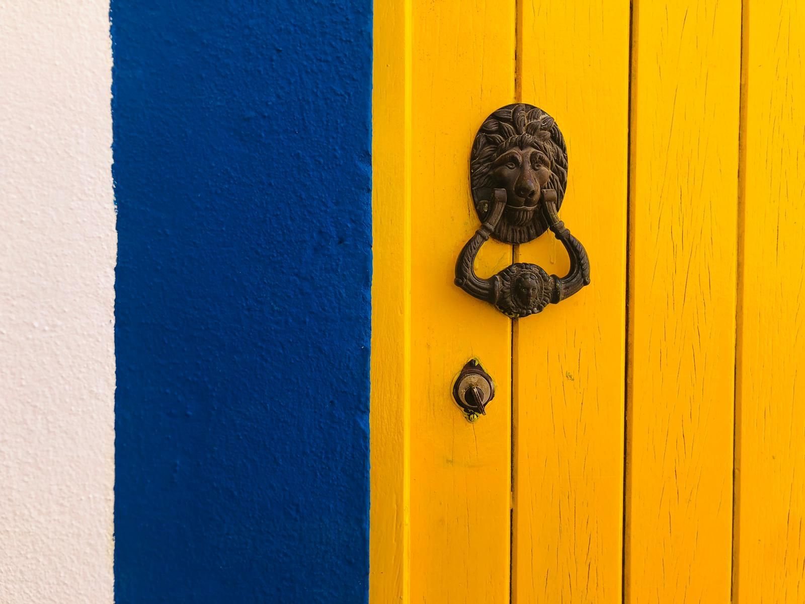 A yellow door with a door knocker on it is next to a blue and white wall.