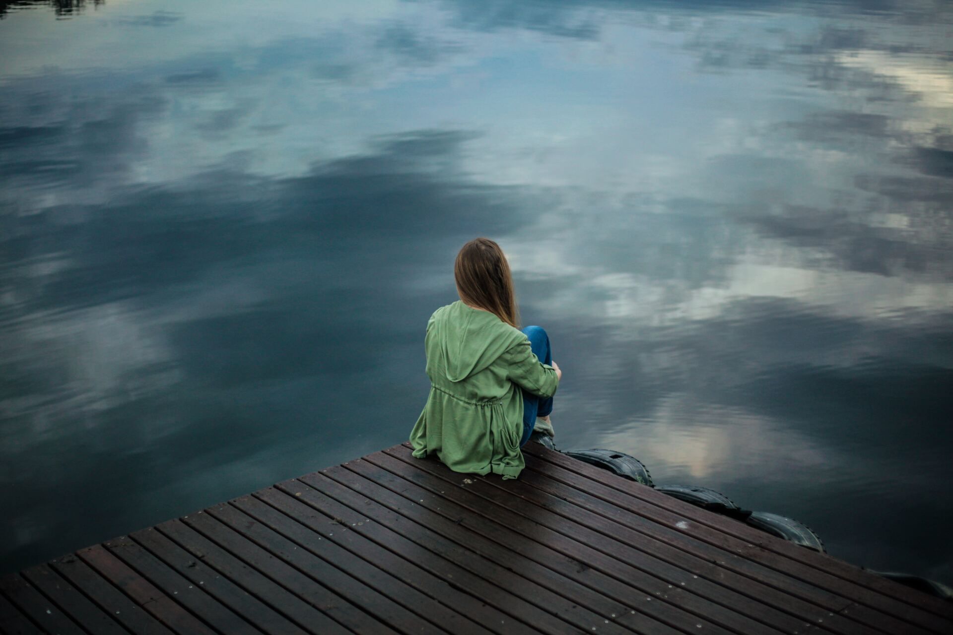 A woman is sitting on a dock looking at the water.