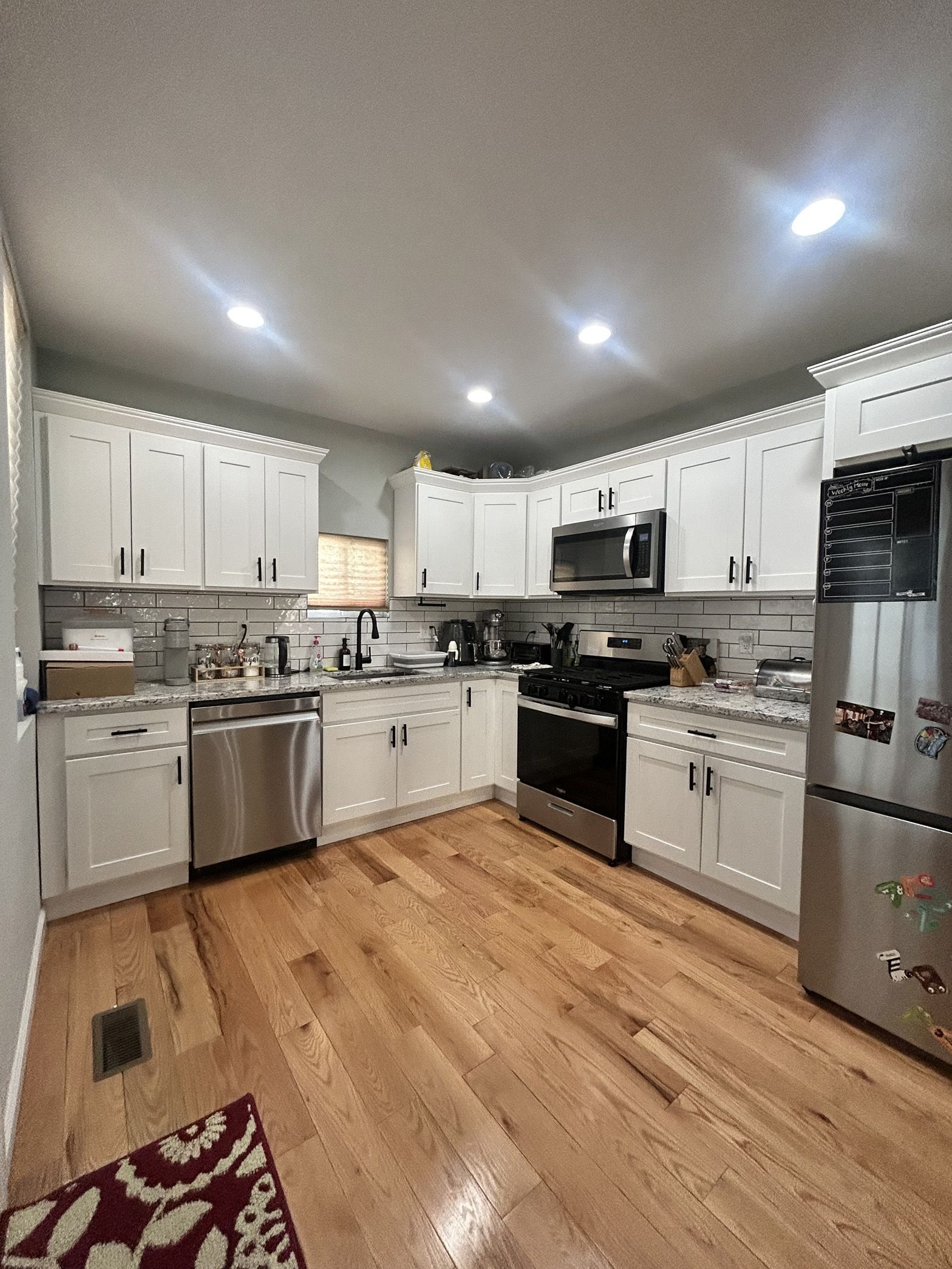 A kitchen with white cabinets , stainless steel appliances , and hardwood floors.