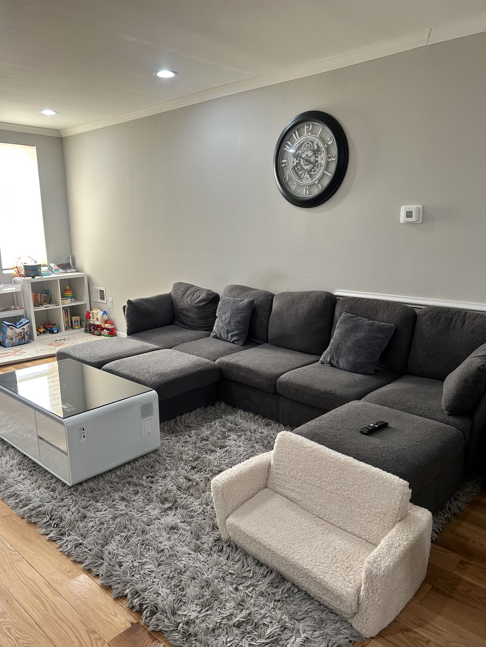 A living room with a couch , coffee table , rug and a clock on the wall.