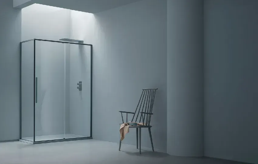 Bagno minimalista con doccia in vetro, pareti grigio chiaro e una sedia in legno con un asciugamano.