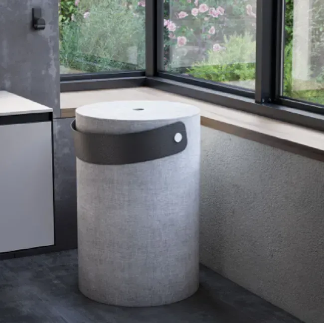 Cesto portabiancheria con una maniglia nera, si trova vicino a una finestra, accanto a un mobiletto.