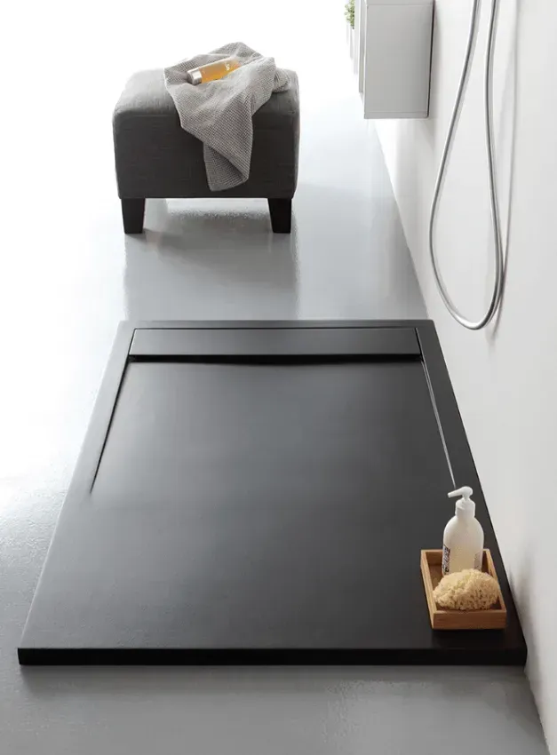 Piatto doccia rettangolare nero con sgabello grigio e accessori in un bagno minimalista.
