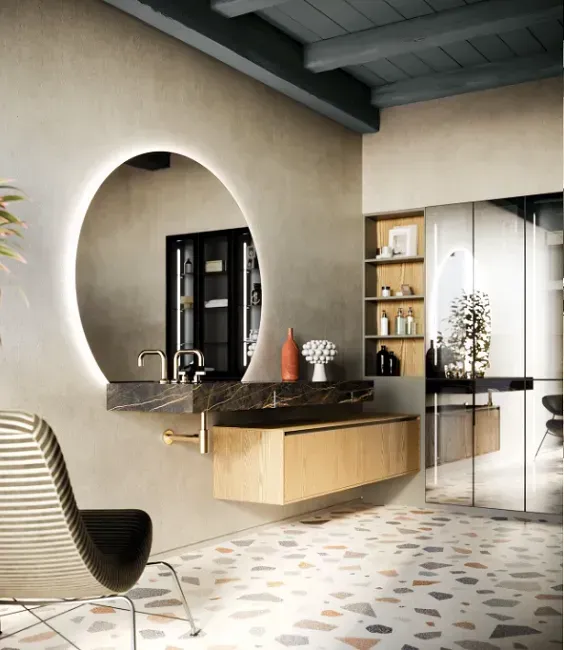 Bagno moderno con specchio rotondo illuminato, mobile lavabo in legno, pavimento in terrazzo e sedia.
