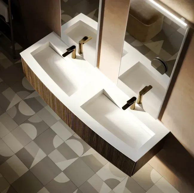 Bagno moderno con doppio lavabo bianco, rubinetti dorati e pavimento in piastrelle fantasia.