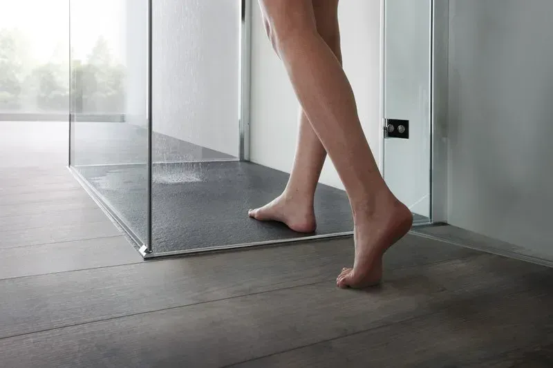 Persona che entra in una doccia moderna con pareti in vetro e pavimento scuro.