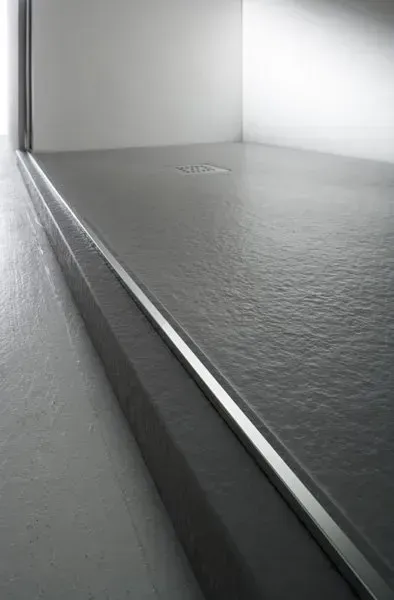 Un pavimento in cemento con uno scarico lineare, pareti grigio chiaro e una porta luminosa e aperta.