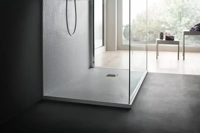 Moderna cabina doccia con pavimento e pareti grigie testurizzate, cabina in vetro e luminosa vista sull'esterno.