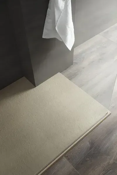 Tappetino da bagno beige sul pavimento in legno del bagno, con un asciugamano bianco appeso e una parete grigia.