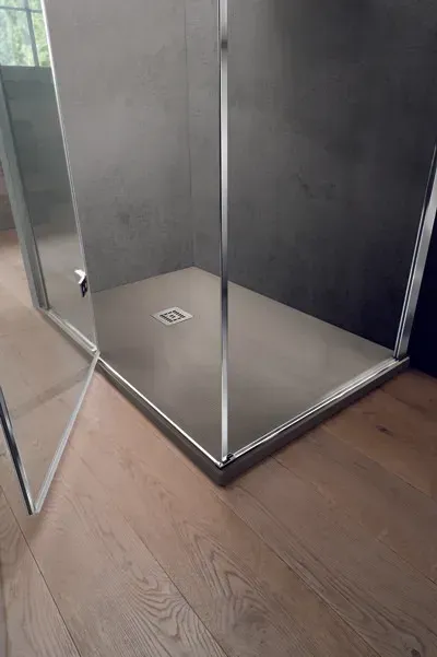 Doccia con pavimento in piastrelle grigie, porte in vetro e finiture argentate, su pavimento in legno.