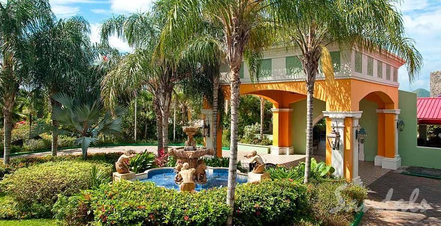 A colorful building with a fountain in front of it surrounded by palm trees.