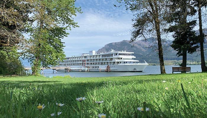 A large cruise ship is docked in a lake surrounded by trees and grass.