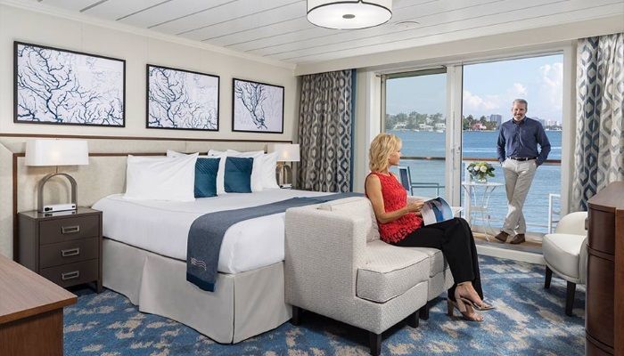 A woman is sitting on a couch in a hotel room next to a bed.