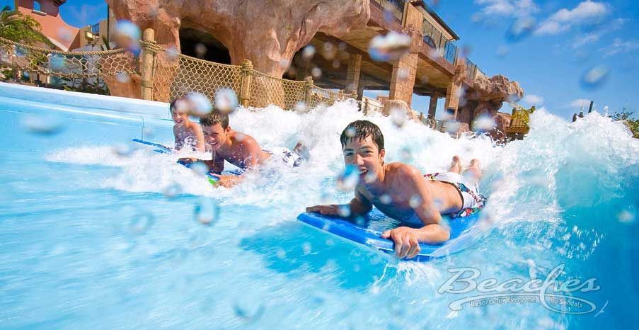 A man is laying on a surfboard in the water at a water park.