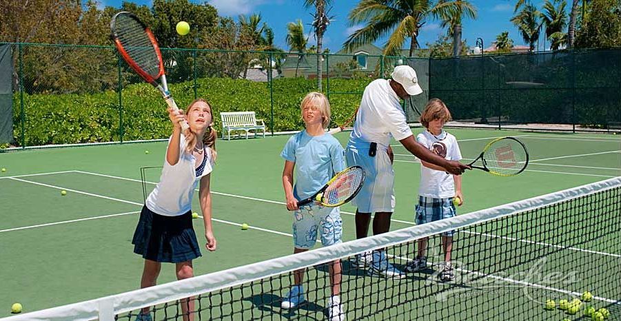 A group of children are playing tennis on a tennis court