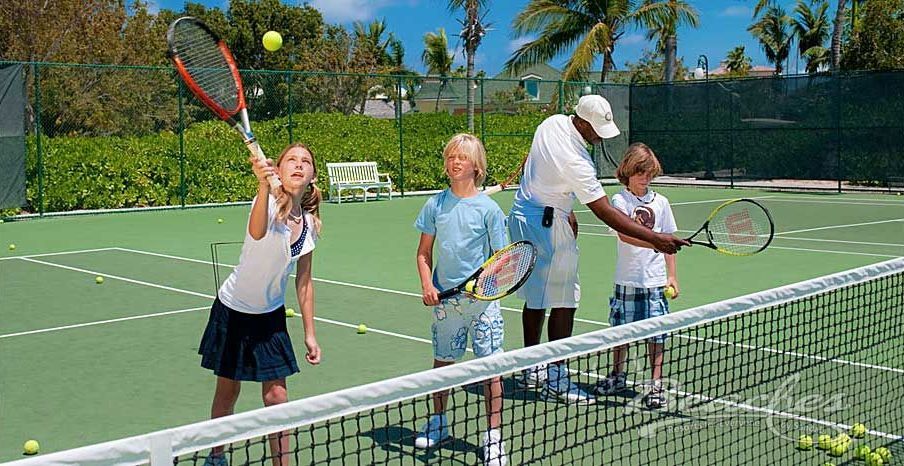 A group of children are playing tennis on a tennis court