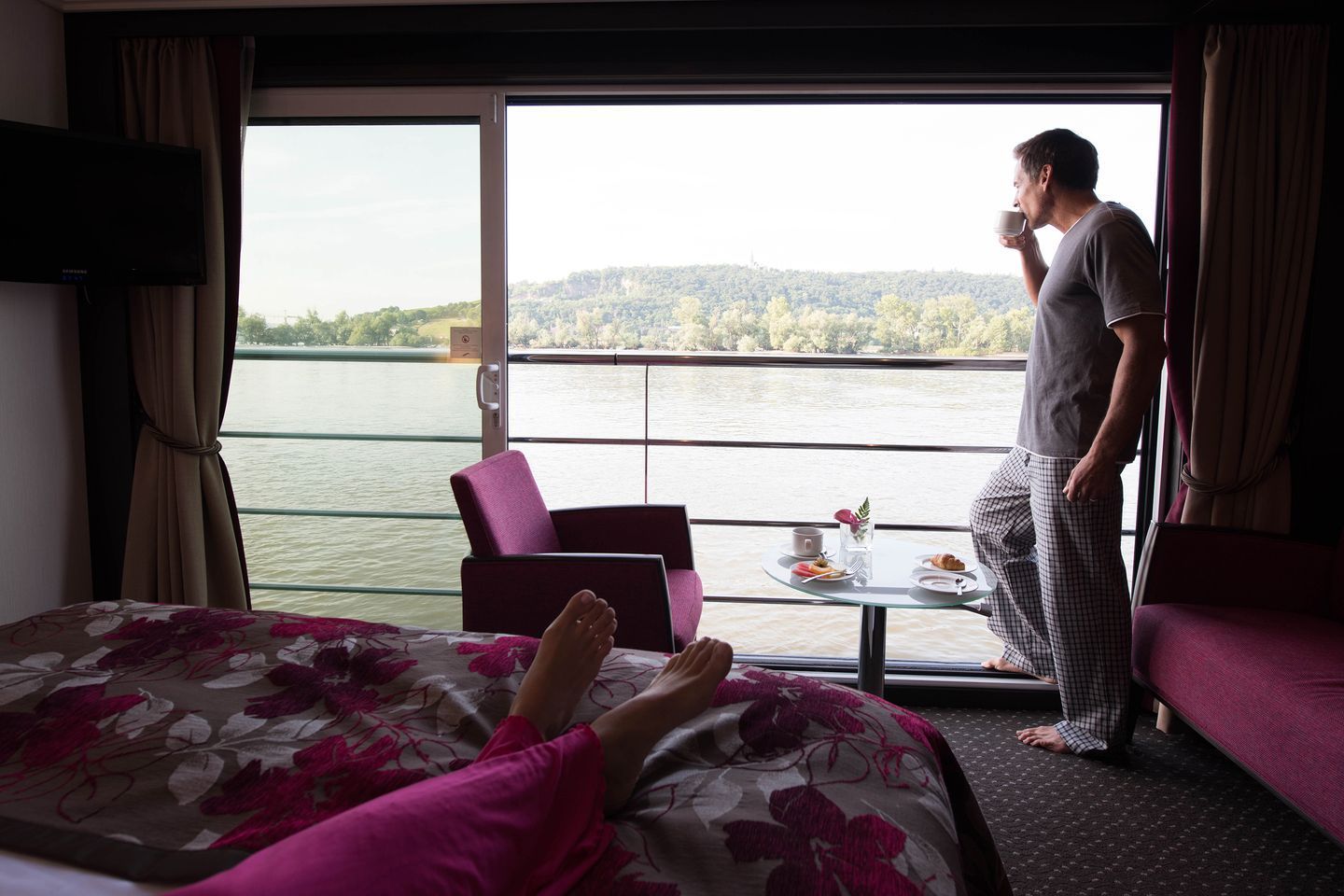 A man standing in front of a window looking out over a body of water
