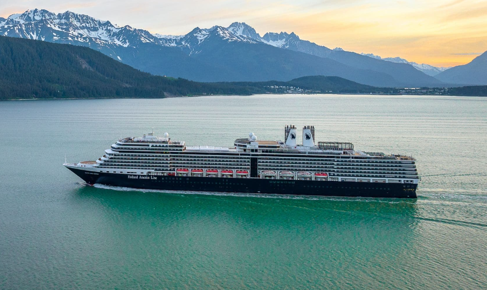 A large cruise ship is floating on top of a body of water with mountains in the background.