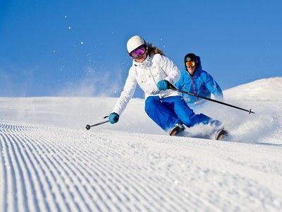 A man and a woman are skiing down a snow covered slope.