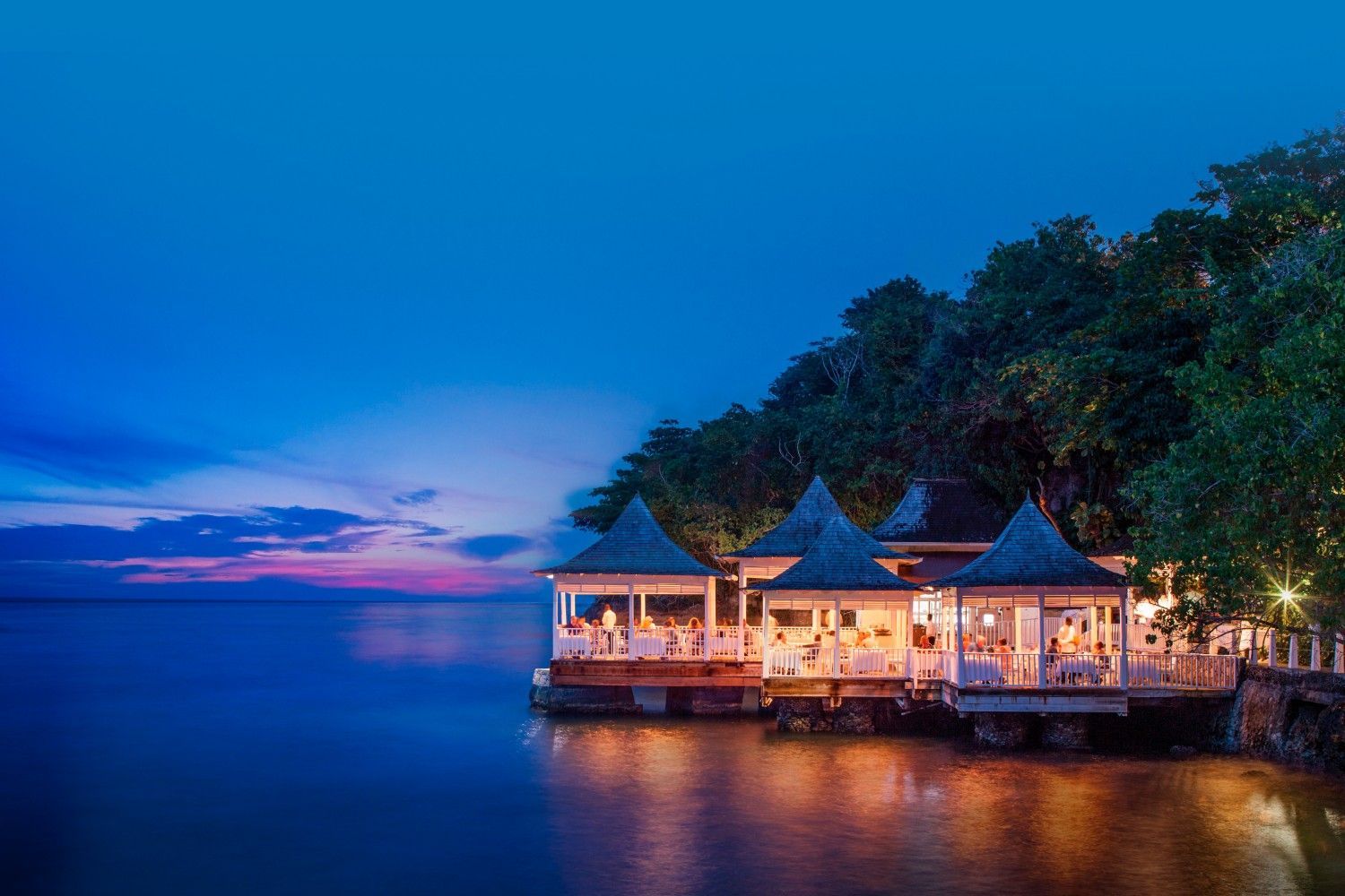 A restaurant on a dock overlooking the ocean at night.